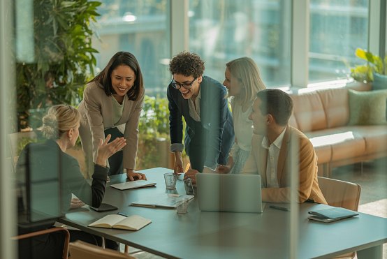A team gathered around a laptop in a glass meeting room